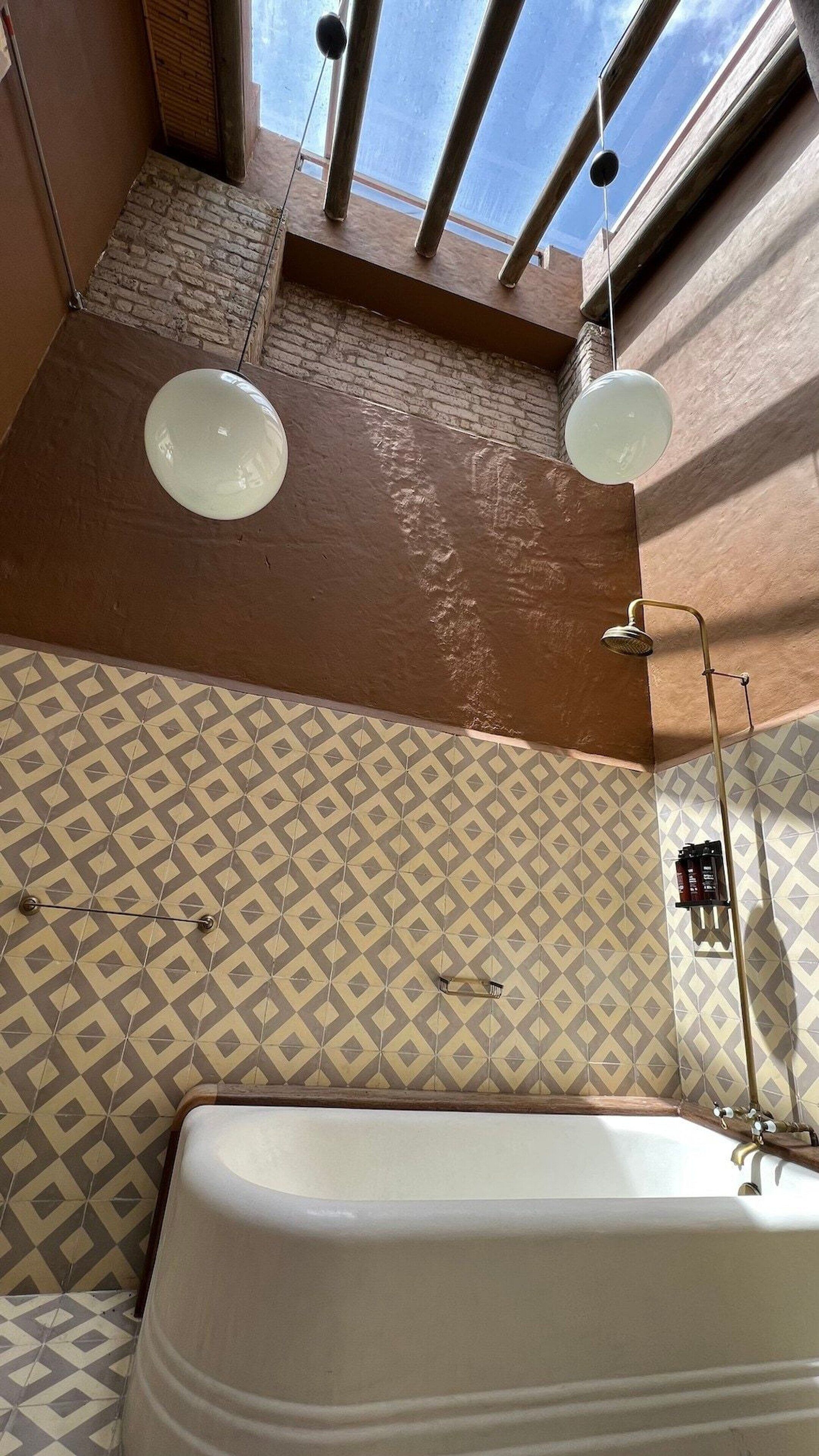 Ein Badezimmer mit einer Badewanne, zwei Wandleuchten, einer gefliesten Rückwand mit Muster und einem Fenster mit Blick.