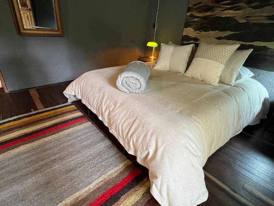 A neatly made bed with a rolled towel, a striped rug, and a nightstand with a lamp.