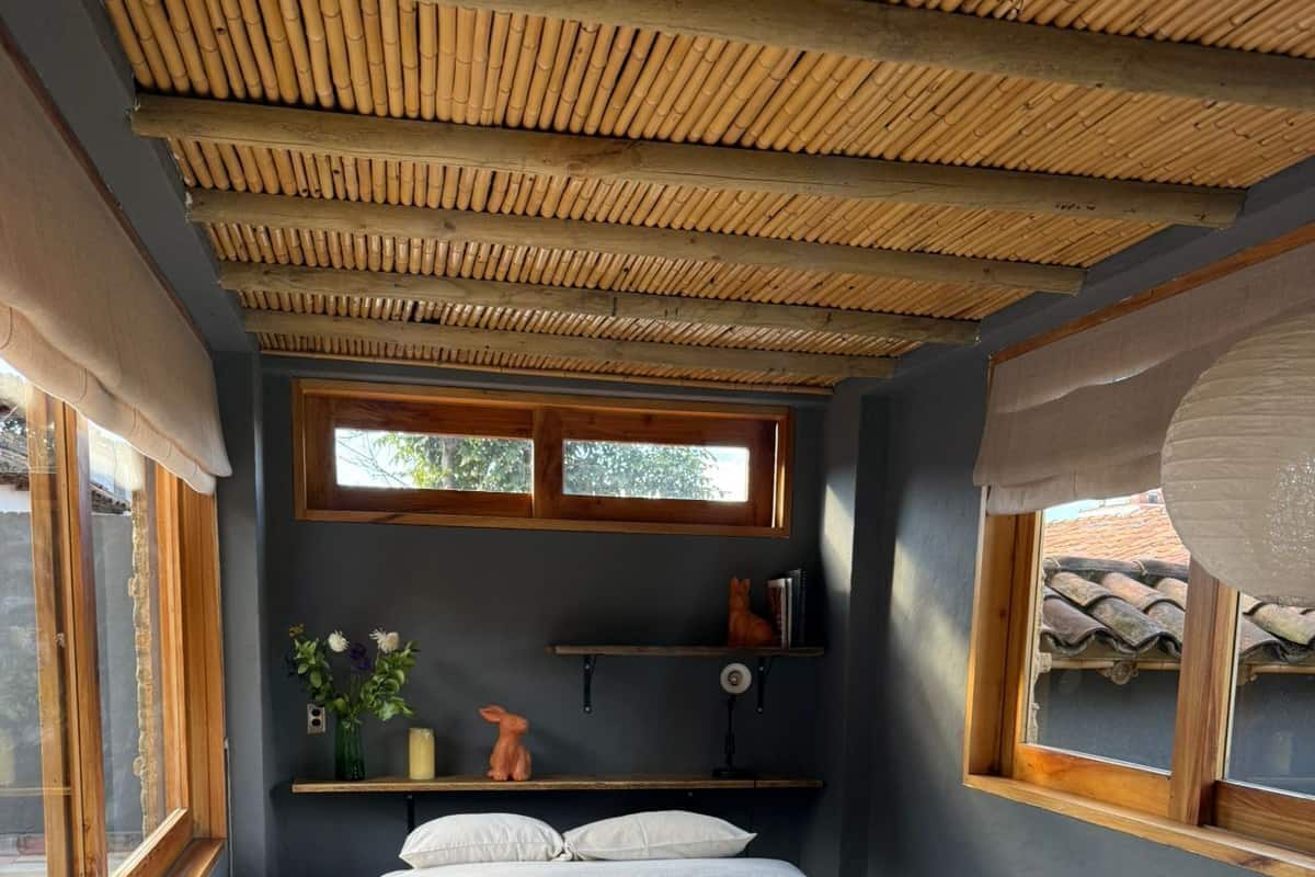 A bedroom with a bed, a window, a shelf with decorative items, and a bamboo ceiling.