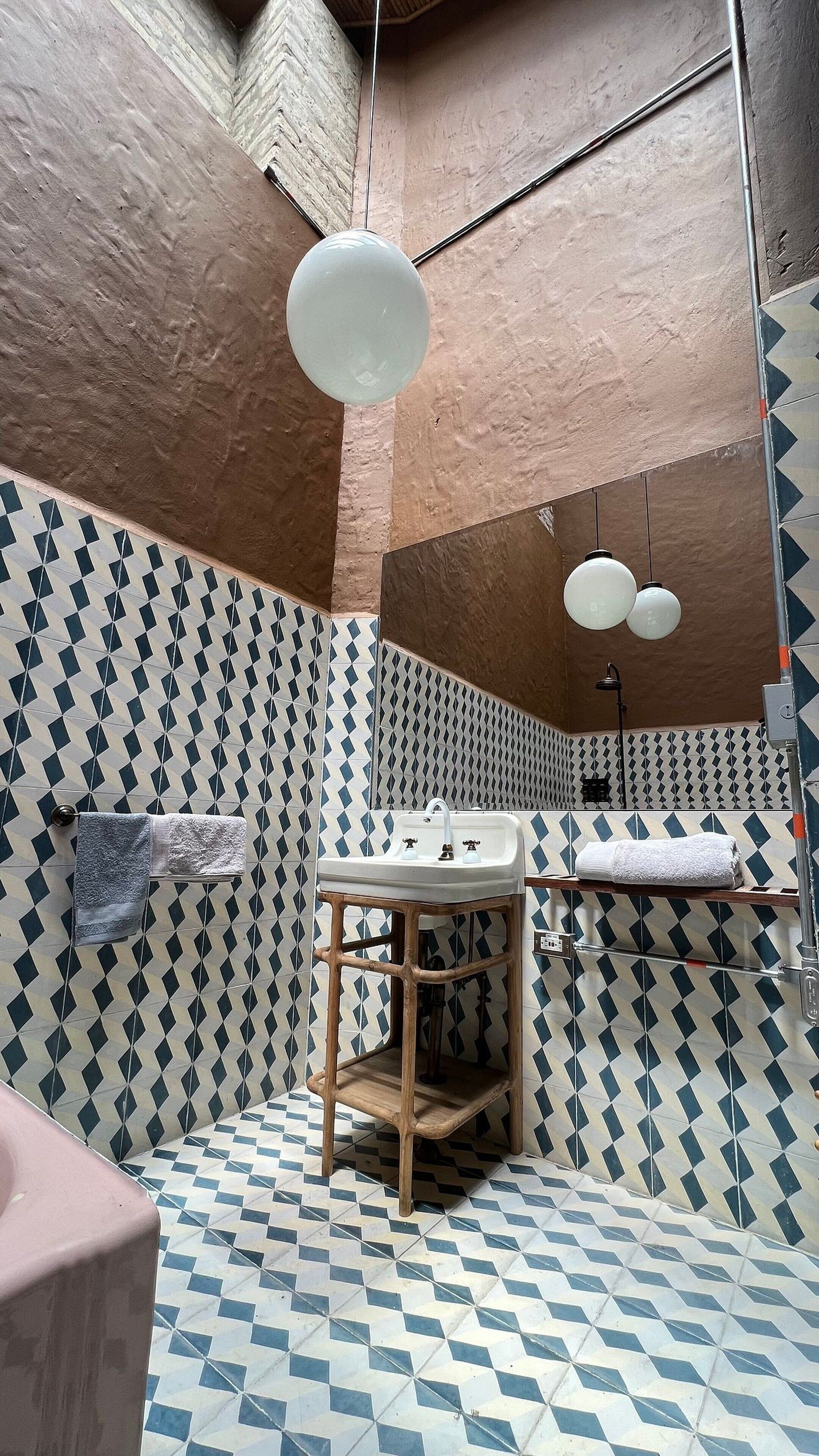 Ein Badezimmer mit gemusterten Fliesen, einem Holzschemel, einem Waschbecken und einem Spiegel.