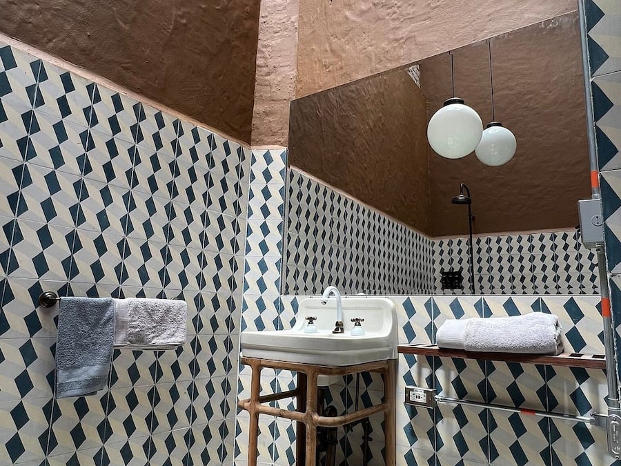 Ein Badezimmer mit gemusterten Fliesen, einem Holzschemel, einem Waschbecken und einem Spiegel.