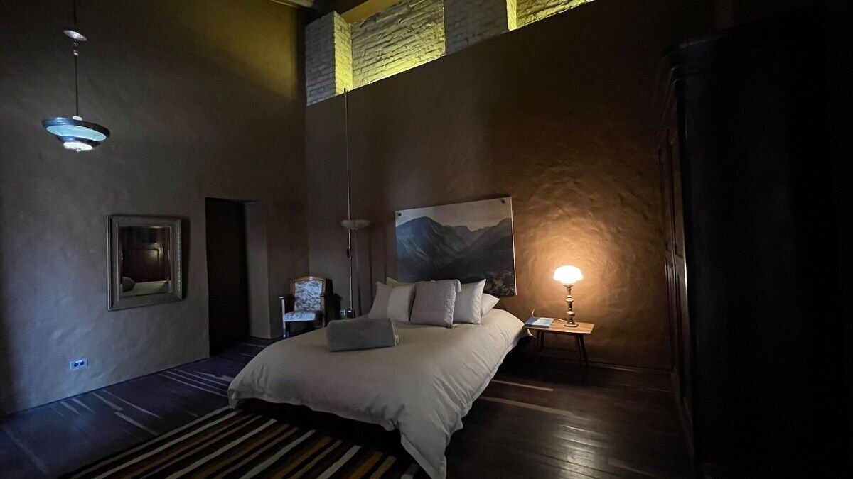 Une chambre à coucher avec un grand lit, une table de chevet, une lampe, un tableau au mur et une fenêtre donnant sur les montagnes.
