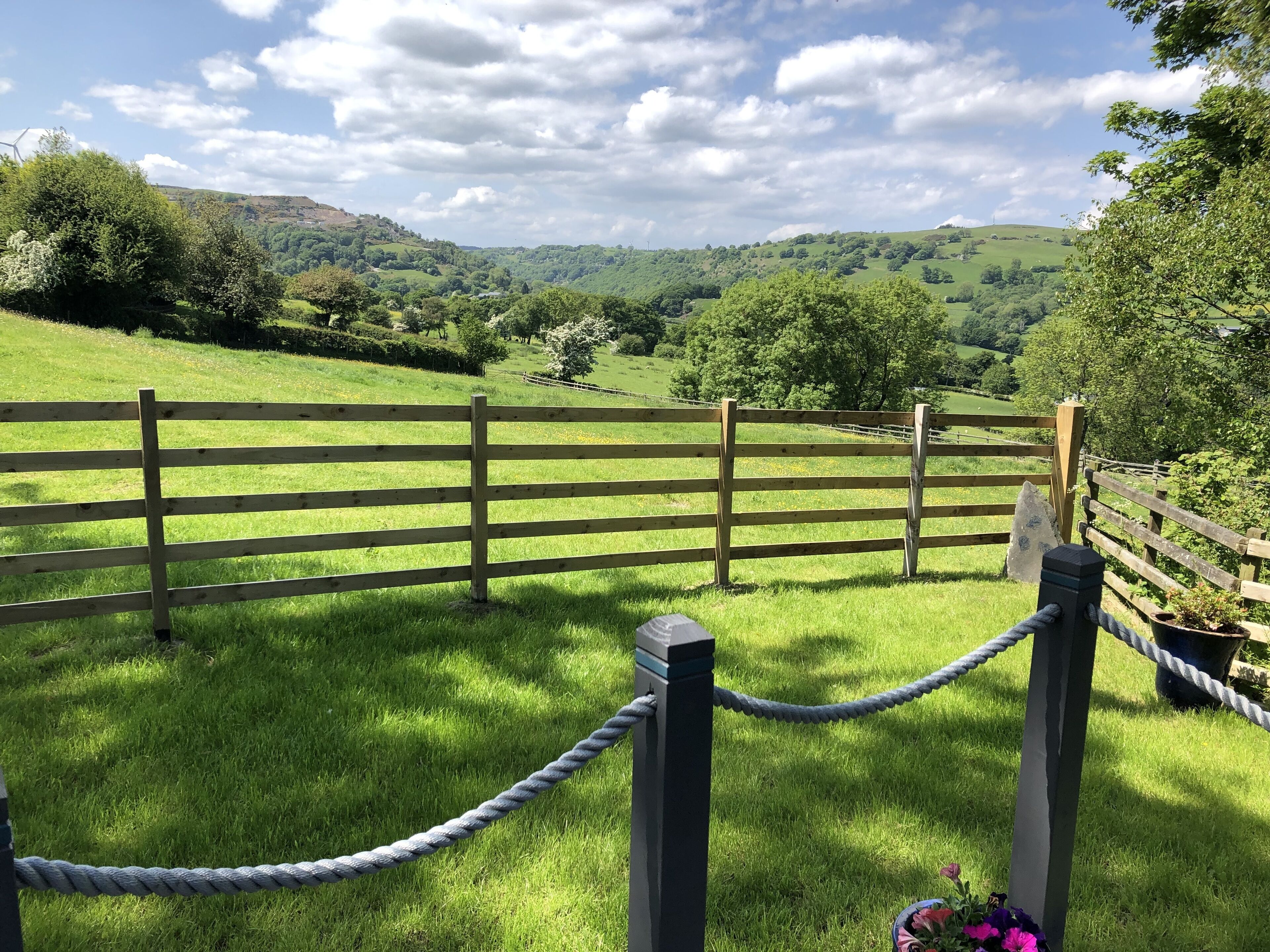 A wooden fence with a rope barrier in a grassy field with a view of rolling hills in the background.