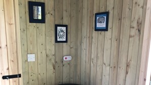 A wooden-paneled room with a black wood stove, two framed pictures on the wall, and a door.