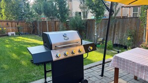Ein Garten mit Grill, Tisch mit kariertem Tischläufer und Holzzaun.