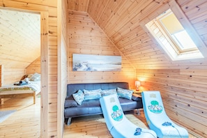 Una cabaña de madera acogedora con habitación en altillo, sofá con cojines estampados y un tobogán para niños.