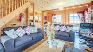 L’intérieur d’un chalet en bois, avec deux canapés gris, une table basse et un fauteuil en cuir noir.