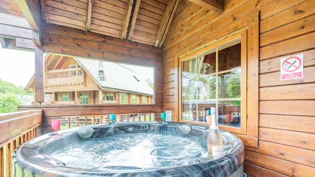 Une cabane en bois avec un jacuzzi, un balcon et un panneau indiquant qu’il est interdit de fumer.
