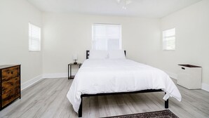 A bedroom with a bed, a ceiling fan, a nightstand, a dresser, and a window with blinds. - Iconic Speedway Location next to Indy 500 track, amenities, and restaurants (Indianapolis)
