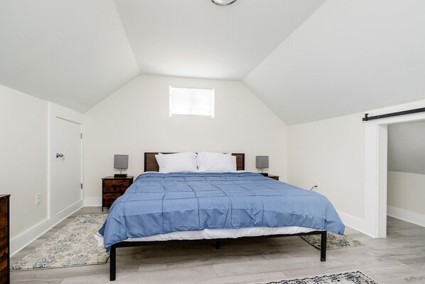 A bedroom with a bed, a nightstand, a lamp, a window, and a door.