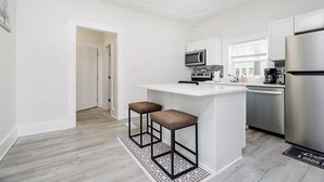 A modern kitchen with white cabinetry, a stainless steel refrigerator, a microwave, and two bar stools. - Iconic Speedway Location next to Indy 500 track, amenities, and restaurants (Indianapolis)