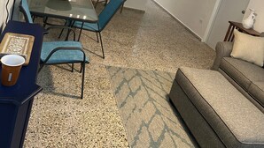 Un espacio habitable compacto con kitchenette, un comedor con sillas azules, un sofá y una alfombra pequeña.
