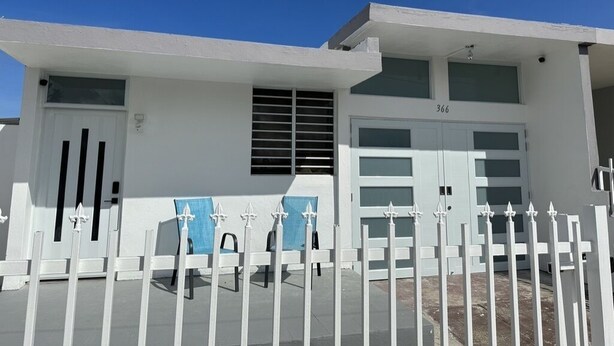 Una casa moderna de dos pisos con fachada blanca, un garaje y un patio delantero cercado.