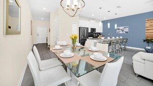 Un espace repas moderne avec une table en verre, des chaises blanches et un luminaire central.