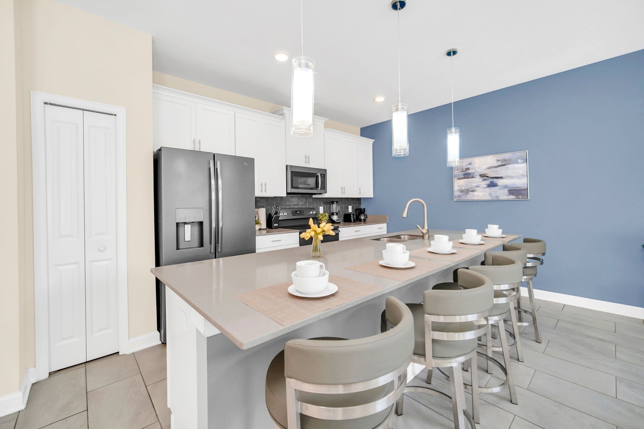 A modern kitchen with white cabinets, a stainless steel refrigerator, a microwave, and a coffee station.
