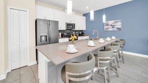 Une cuisine moderne avec des meubles blancs, un réfrigérateur en acier inoxydable, un four à micro-ondes et un coin café.