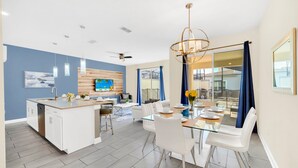 Une cuisine moderne dotée d’un îlot central, un coin repas avec une table en verre et un espace de vie avec une grande fenêtre.