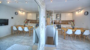 Une cuisine moderne avec des armoires blanches, un comptoir en bois et un four encastré. On y trouve également un coin repas avec une table en bois et des chaises blanches.