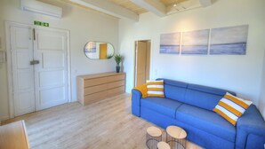 Une pièce avec un canapé bleu, un plancher en bois, un miroir, une plante et un tableau accroché au mur.