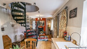 A cozy kitchen with a spiral staircase, wooden flooring, and a dining area with a table set for two. - The Cottage (Stratford-upon-Avon)