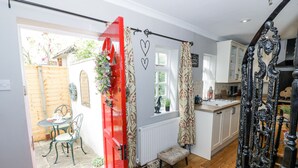 A kitchen with wooden flooring, a red door, and a small dining area with a table and chairs. - The Cottage (Stratford-upon-Avon)