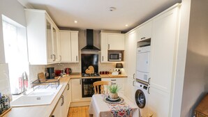 A compact kitchen with white cabinets, a microwave, a stove, and a washing machine. - The Cottage (Stratford-upon-Avon)