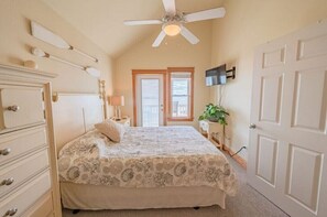 A bedroom with a bed, dresser, ceiling fan, and a door. - Sound front condo, pool, water access, & sunsets (Nags Head)