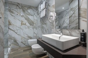 A modern bathroom with a large white sink, a glass shower enclosure, and a marble-tiled wall.