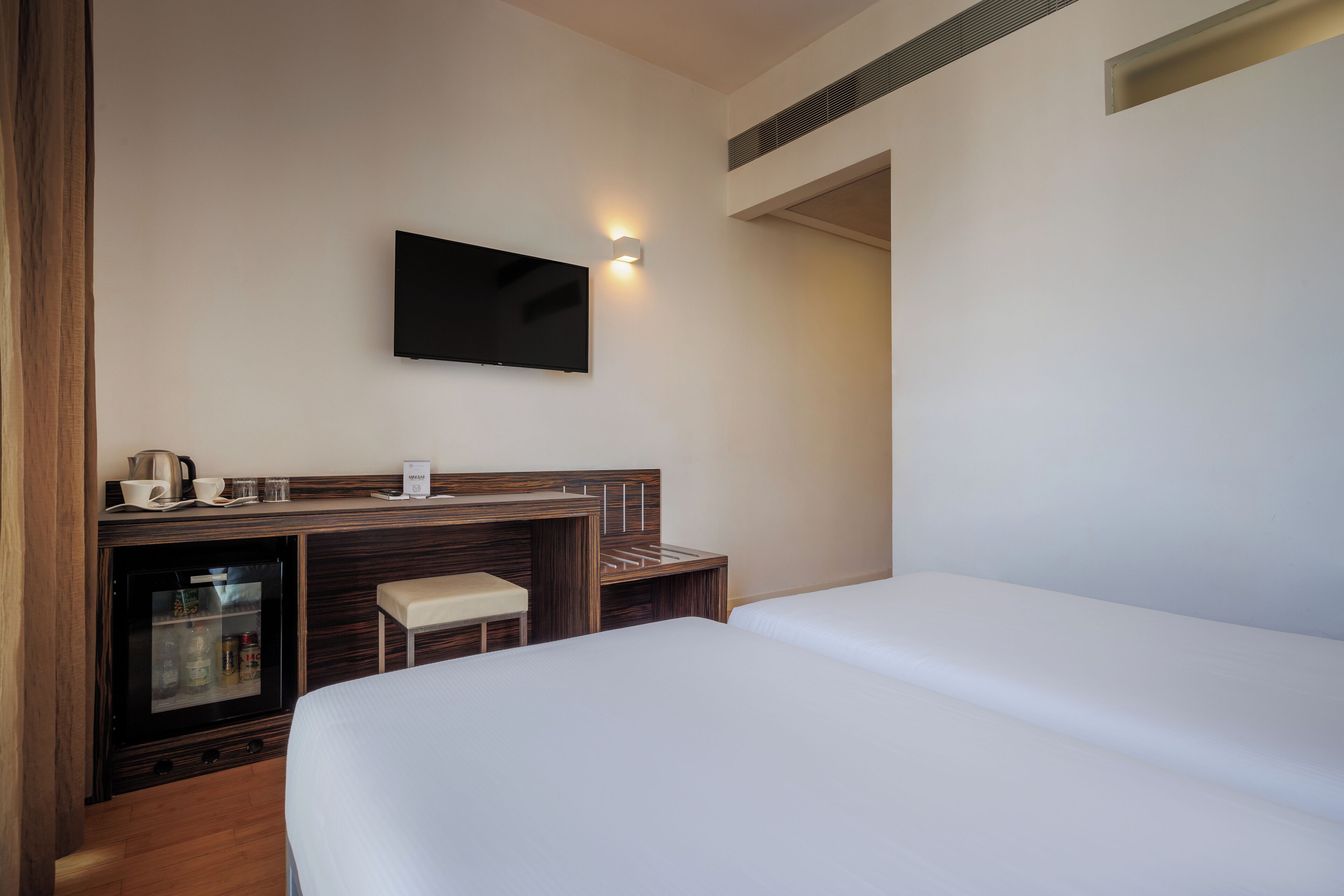 Egy szállodai szoba, amelyben található egy ágy, egy íróasztal televízióval, egy minibar és egy kis ülősarok.
