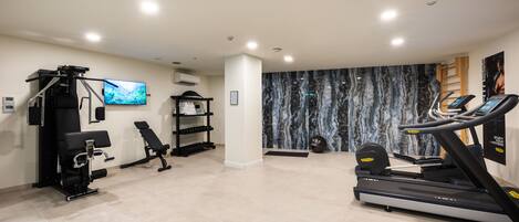 A modern gym with exercise equipment, a television, and a marble-patterned wall.