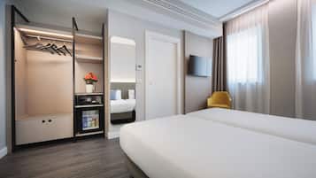 Habitación de hotel con cama, armario, zona de estar, televisión y ventana con cortinas.