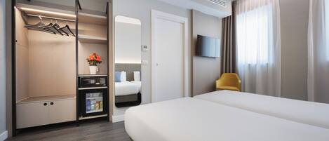 Habitación de hotel con cama, armario, zona de estar, televisión y ventana con cortinas.