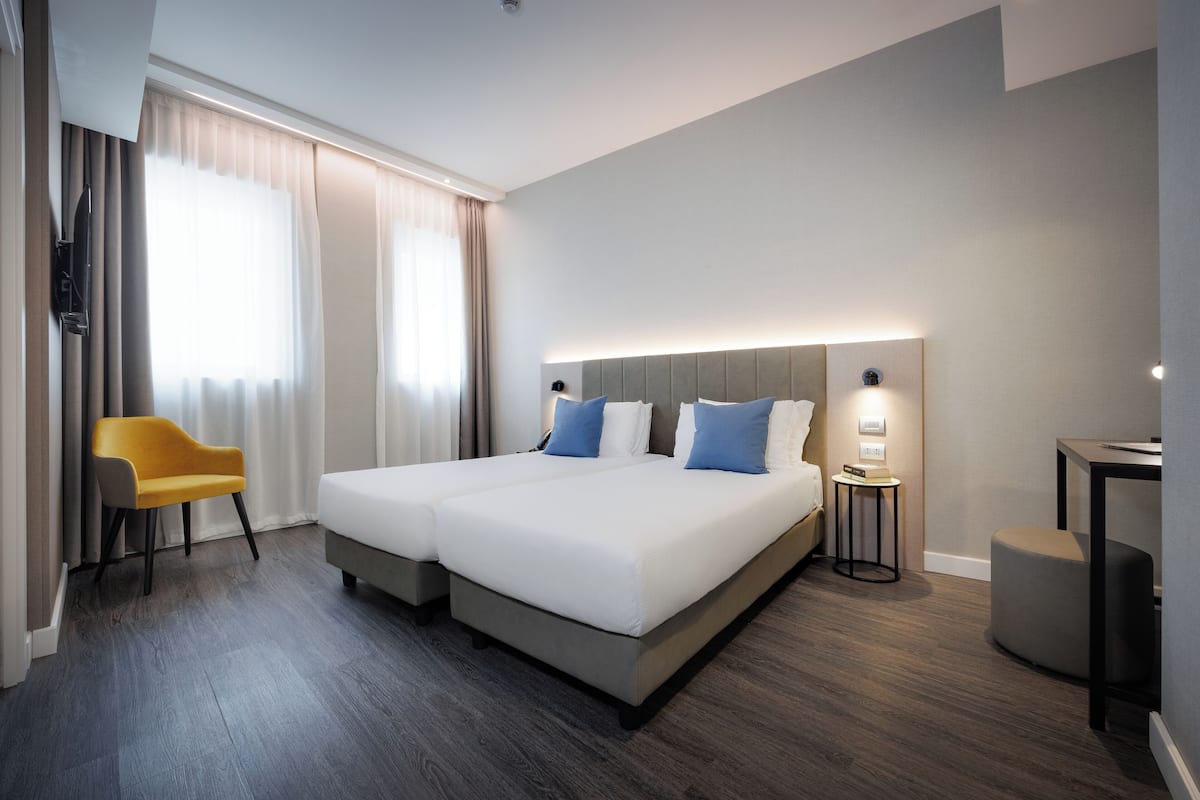 A modern hotel room with a large bed, a small desk, a chair, and a TV.