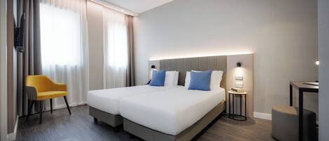Et moderne hotelværelse med en stor seng, et lille skrivebord, en stol og et fjernsyn.