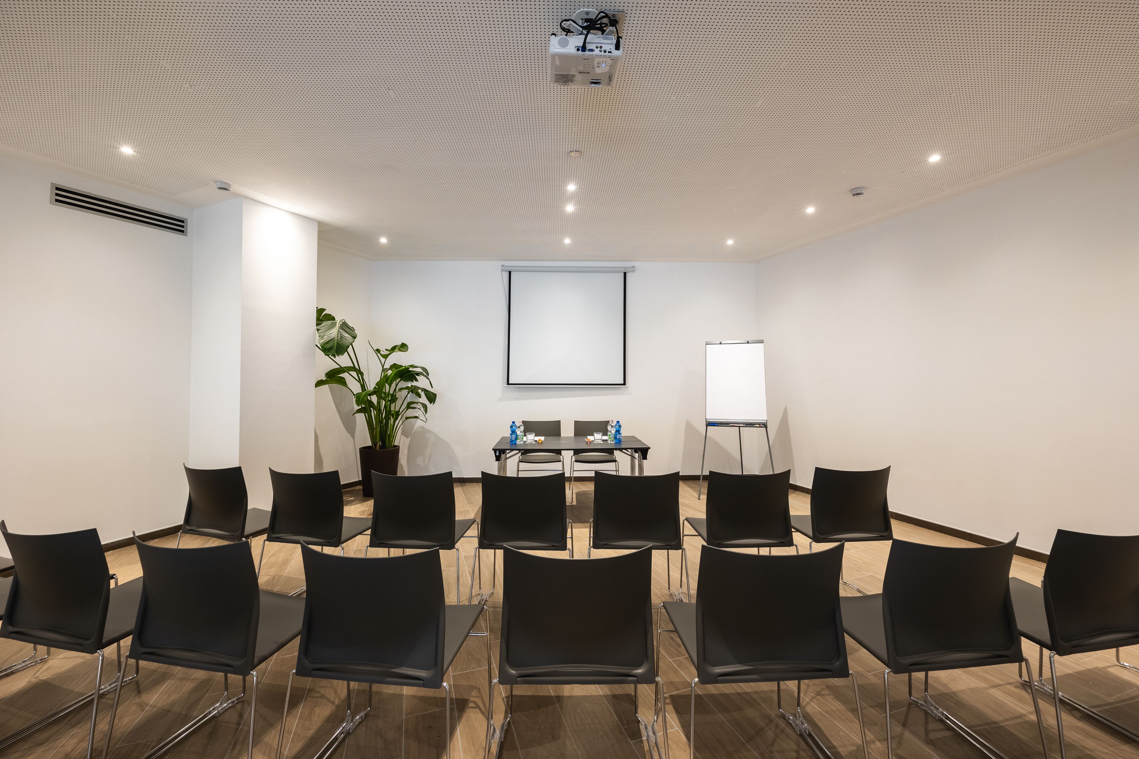 A conference room with a projector, whiteboard, and a potted plant.