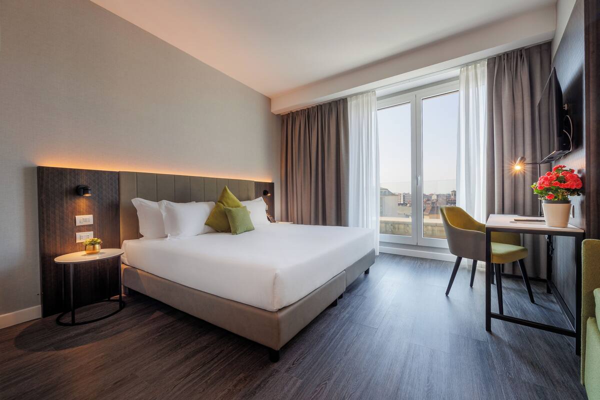 A modern hotel room with a large bed, a desk, and a view of the city.