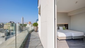 A modern hotel room with a balcony overlooking a cityscape, a large potted plant, and a neatly made bed. - IH Hotels Milano Centrale (Milan)