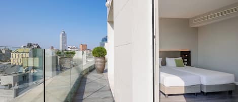 A modern hotel room with a balcony overlooking a cityscape, a large potted plant, and a neatly made bed.