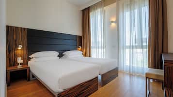 Hotelkamer met twee bedden, houten vloeren, een donker hoofdeinde en uitzicht op het landschap door dunne gordijnen.
