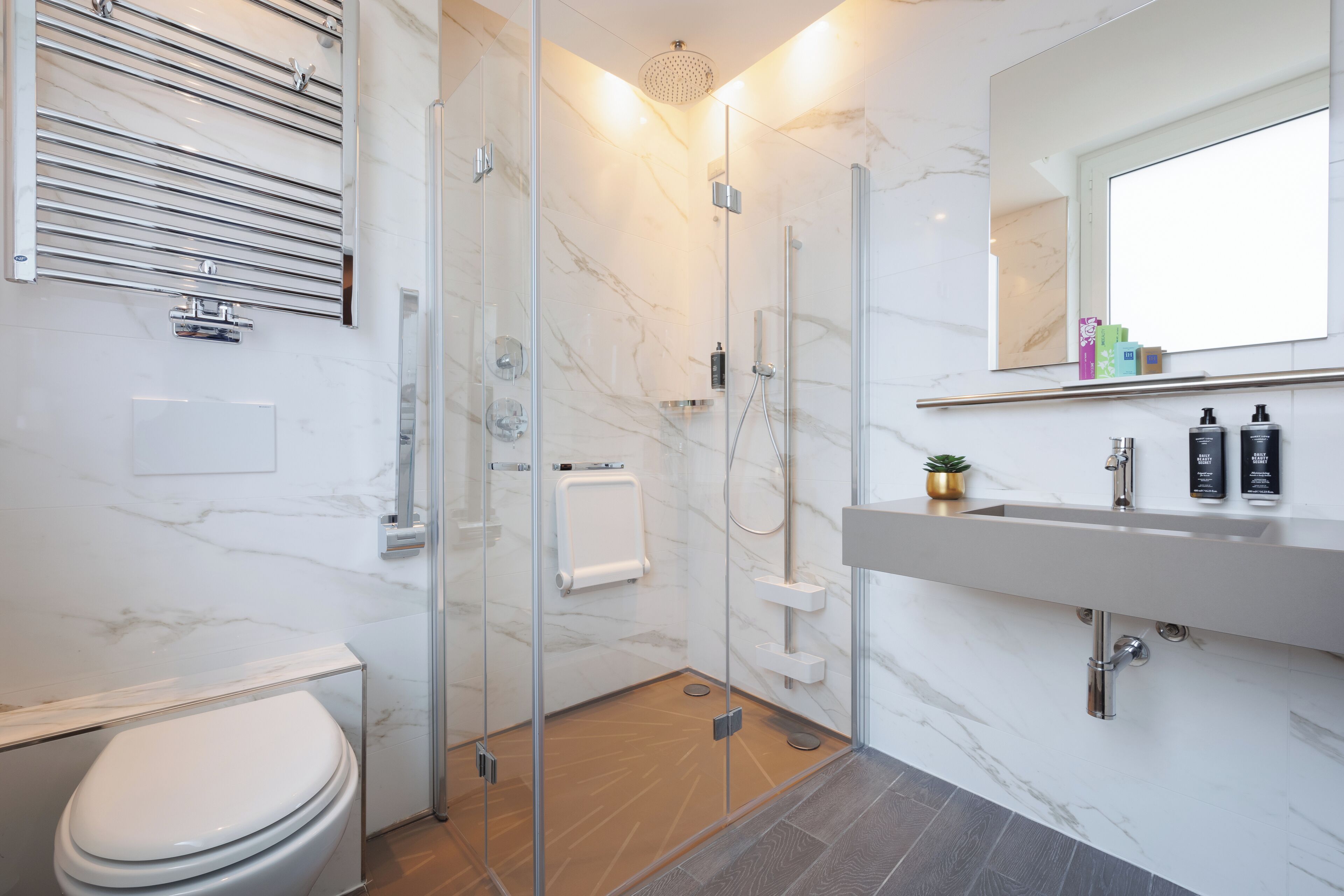 Une salle de bain moderne avec une douche à parois de verre, des toilettes blanches, un sol carrelé en marbre et un lavabo avec des articles de toilette.