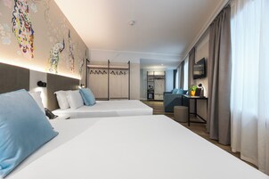 A hotel room with two beds, a desk, a TV, and a bathroom in the background.
