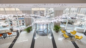 A spacious lobby with a central elevator, multiple seating areas, and a view of parked cars outside. - IH Hotels Milano Centrale (Milan)