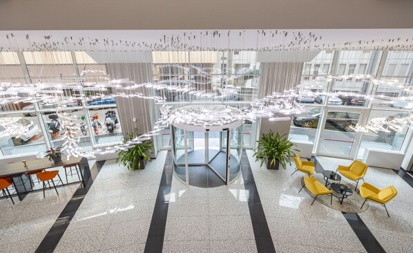 A spacious lobby with a central elevator, multiple seating areas, and a view of parked cars outside. - IH Hotels Milano Centrale (Milan)