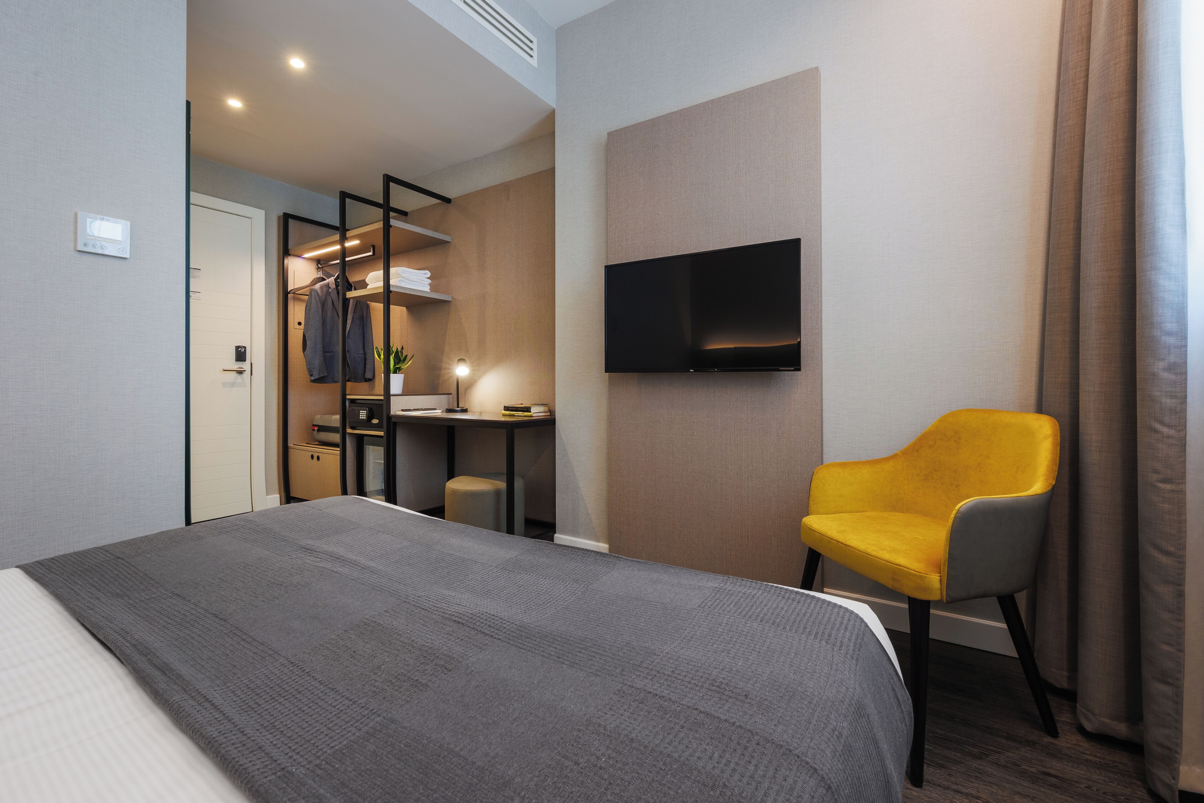 Ein Hotelzimmer mit Bett, Schreibtisch, Stuhl, Fernseher und Kleiderschrank.