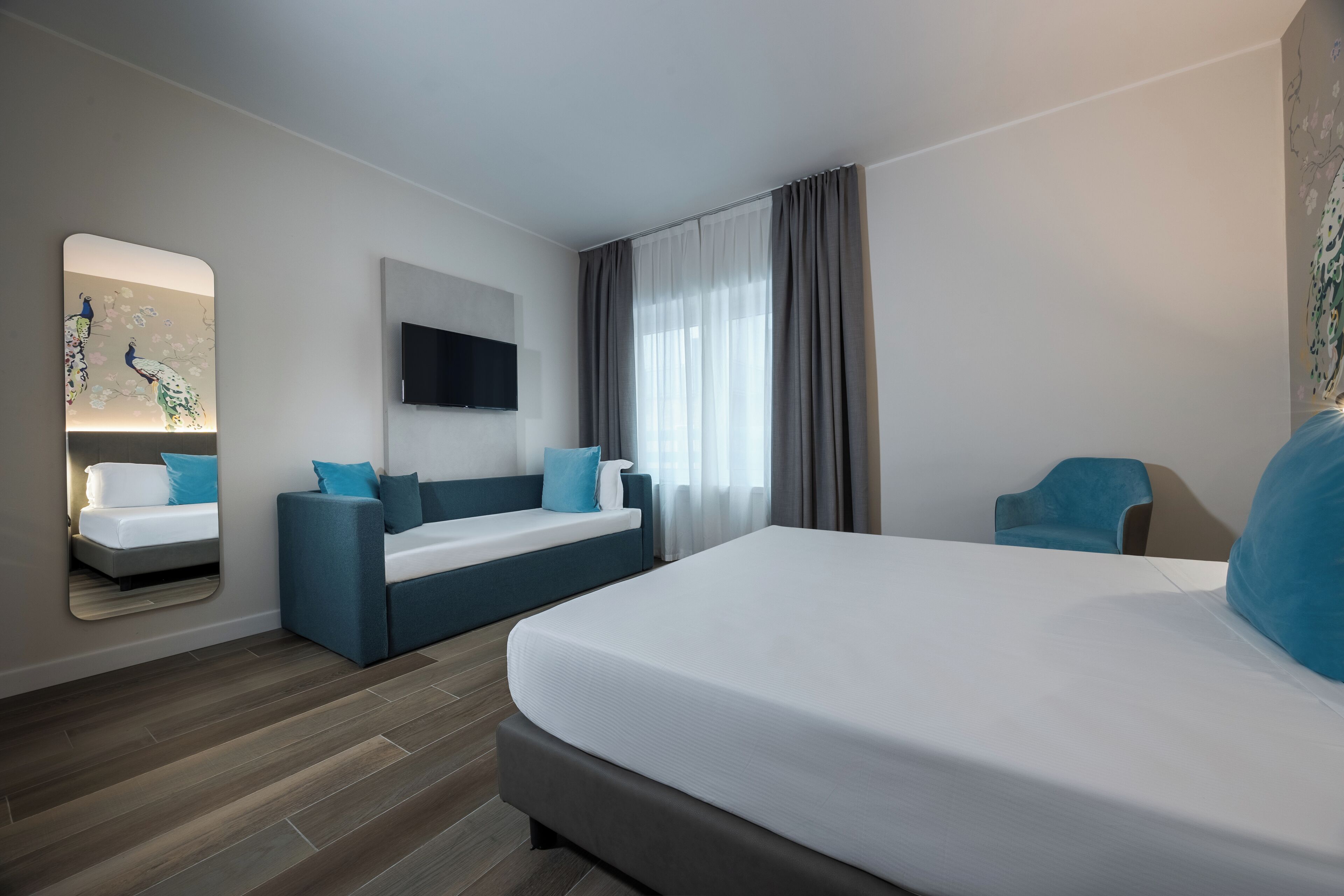 A modern hotel room with a large bed, a sofa, a TV, and a mirror.