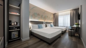 A modern hotel room with two beds, a minibar, a desk with a chair, and a large window with curtains. - IH Hotels Milano Centrale (Milan)