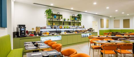 Un restaurante moderno con asientos verdes y naranja, una barra central con una máquina de café y plantas en macetas sobre estantes.