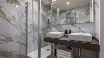 Een moderne badkamer met marmeren wanden, een glazen douchecabine en twee wastafels met kraanwerk.