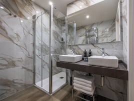 Un baño moderno con paredes de mármol, cabina de ducha de vidrio y dos lavamanos.