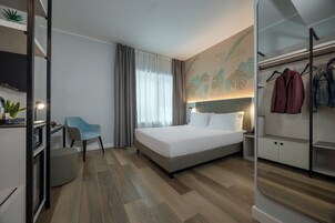 Een moderne hotelkamer met een bed, een bureau, een stoel, een kledingkast en een groot raam met gordijnen.